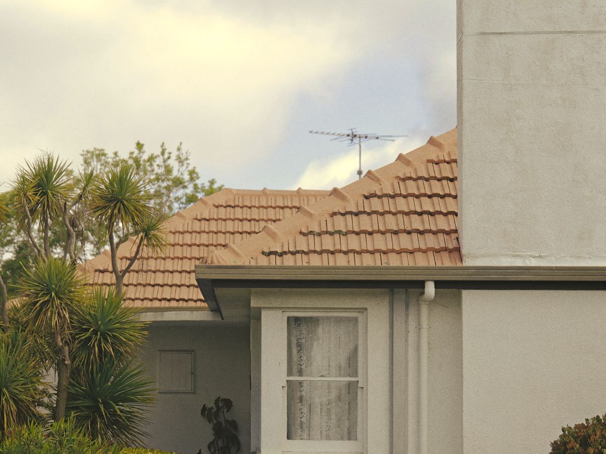 A rendered brick house with a terracotta tile roof and a front lawn